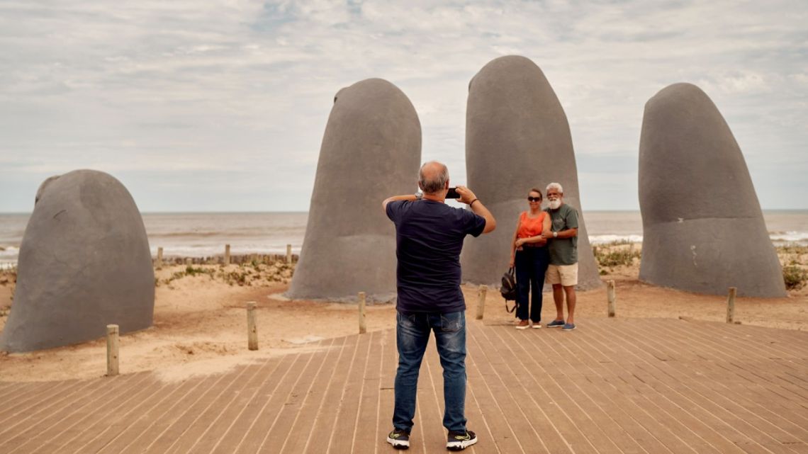 Tourists take photos in front of a sculpture of a giant hand emerging from the sand on Brava Beach in Punta del Este, Uruguay, on Saturday, Nov. 19, 2022.