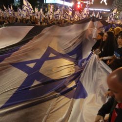 Manifestantes levantan una gran bandera nacional durante una concentración para protestar contra el proyecto de ley de reforma judicial del gobierno israelí en Tel Aviv. | Foto:JACK GUEZ / AFP