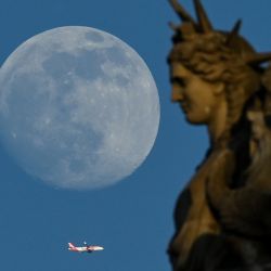 Un avión vuela junto a una estatua del Louvre mientras sale la luna gibosa creciente en París, Francia. | Foto:STEFANO RELLANDINI / AFP