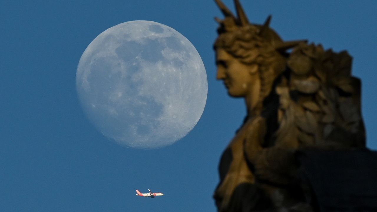 Un avión vuela junto a una estatua del Louvre mientras sale la luna gibosa creciente en París, Francia. | Foto:STEFANO RELLANDINI / AFP