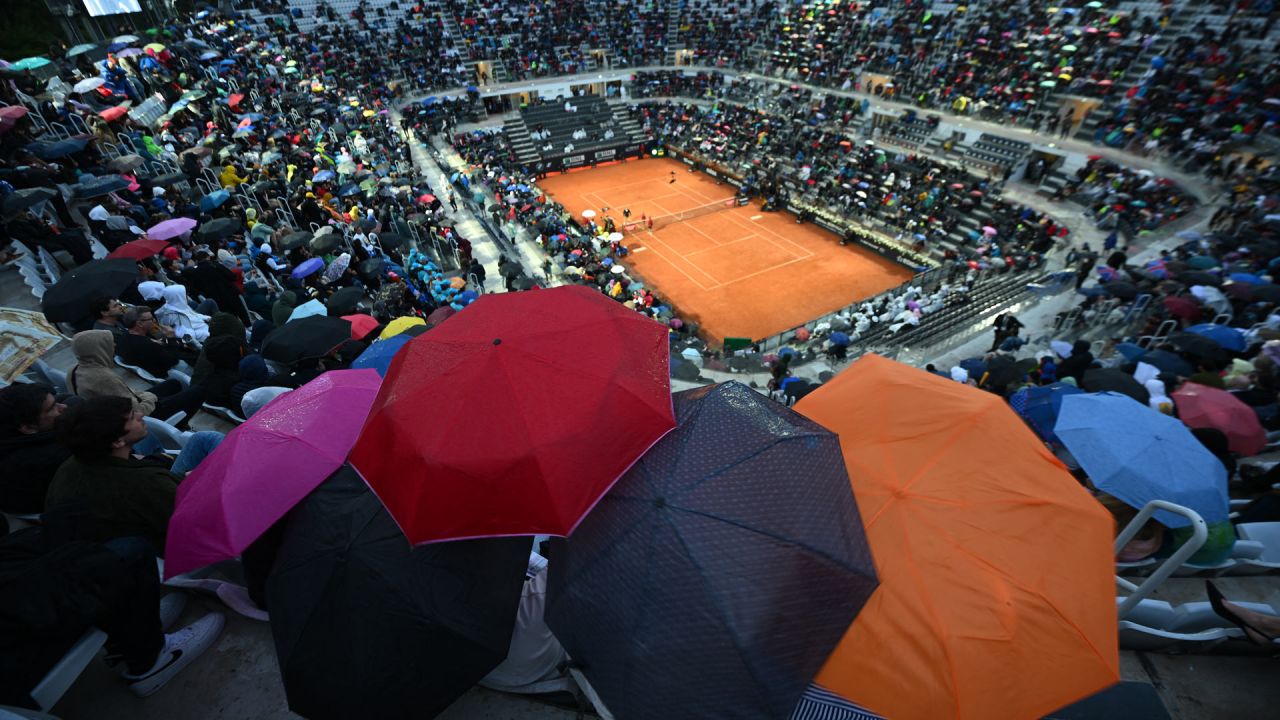 Espectadores en la Pista Central se protegen mientras la lluvia interrumpe la tercera ronda del torneo de tenis masculino ATP Rome Open entre el griego Stefanos Tsitsipas y el italiano Lorenzo Sonego en el Foro Itálico de Roma. | Foto:FILIPPO MONTEFORTE / AFP
