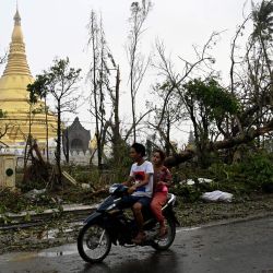 Personas conducen una motocicleta junto a árboles rotos al lado de un templo en Sittwe, en el estado de Rakhine, Myanmar, después de que el ciclón Mocha tocara tierra. | Foto:Sai Aung Main / AFP