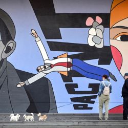 Varias personas pasean a sus mascotas delante de un cartel en una pared de la Casa Central de Artistas, en el centro de Moscú, Rusia. | Foto:ALEXANDER NEMENOV / AFP