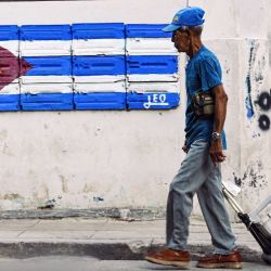 Un anciano pasa junto a un muro con una bandera cubana pintada en La Habana. | Foto:YAMIL LAGE / AFP