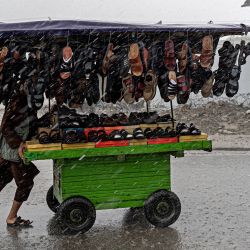 Un vendedor afgano empuja un carro de calzado por una calle mientras llueve en Kabul. | Foto:WAKIL KOHSAR / AFP