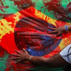 Indígenas sostienen una bandera brasileña manchada con sangre falsa durante una manifestación contra la llamada tesis legal Marco Temporal, un proyecto de ley que detiene la demarcación de territorios indígenas, frente al Congreso Nacional en Brasilia, Brasil. | Foto:Sergio Lima / AFP