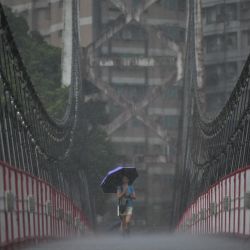 Una mujer usa un paraguas para protegerse de la lluvia mientras camina a lo largo de un puente colgante en la ciudad de Nuevo Taipéi mientras se acerca el tifón Mawar en la costa este de Taiwán. | Foto:Sam Yeh / AFP