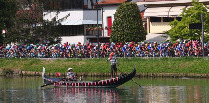 El pelotón de ciclistas pasa junto a dos hombres que conducen una góndola en un canal de la ciudad de Jesolo durante la decimoséptima etapa del Giro de Italia 2023, de 197 km entre Pergine Valsugana y Caorle, cerca de Venecia.