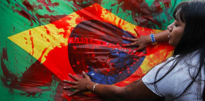 Indígenas sostienen una bandera brasileña manchada con sangre falsa durante una manifestación contra la llamada tesis legal Marco Temporal, un proyecto de ley que detiene la demarcación de territorios indígenas, frente al Congreso Nacional en Brasilia, Brasil.