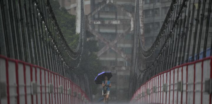 Una mujer usa un paraguas para protegerse de la lluvia mientras camina a lo largo de un puente colgante en la ciudad de Nuevo Taipéi mientras se acerca el tifón Mawar en la costa este de Taiwán.