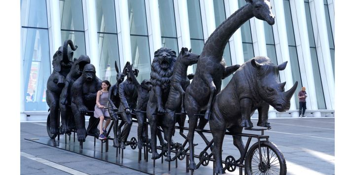 Una persona se sienta sobre una escultura de bronce de los artistas Gillie y Marc titulada "They were on a wild ride to a safer place with Rabbitwoman and Dogman", que forma parte de la exposición "A Wild Life For Wildlife" en el Oculus Center de Nueva York.