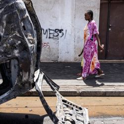 Una mujer pasa junto a un coche quemado en Dakar, mientras se calman las protestas cuatro días después de que un tribunal de Senegal condenara al líder de la oposición Ousmane Sonko, candidato a las elecciones presidenciales de 2024, a dos años de prisión acusado de "corromper a la juventud", pero le absolviera de violación y de proferir amenazas de muerte. | Foto:JOHN WESSELS / AFP