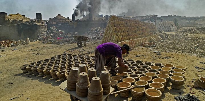 Un trabajador apila vasijas mientras sale humo de un horno en Karachi, Pakistán.