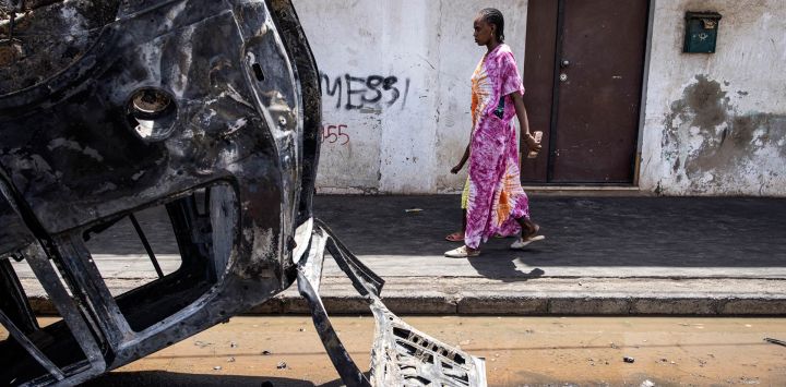 Una mujer pasa junto a un coche quemado en Dakar, mientras se calman las protestas cuatro días después de que un tribunal de Senegal condenara al líder de la oposición Ousmane Sonko, candidato a las elecciones presidenciales de 2024, a dos años de prisión acusado de "corromper a la juventud", pero le absolviera de violación y de proferir amenazas de muerte.