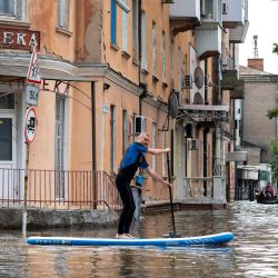 Un residente local navega en una tabla de sup durante una evacuación de una zona inundada en Kherson, tras los daños sufridos en la presa de la central hidroeléctrica de Kakhovka. El presidente ucraniano, Volodymyr Zelensky, visitó la región inundada por la rotura de la presa de Kakhovka, mientras el gobernador regional declaraba que 600 kilómetros cuadrados estaban bajo el agua. | Foto:ALEKSEY FILIPPOV / AFP