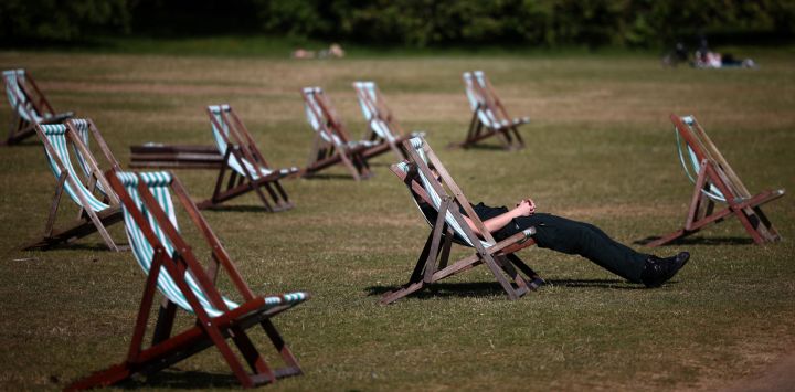 Personas sentadas en reposeras sobre hierba seca de color marrón, bajo el sol en Hyde Park, en el centro de Londres.