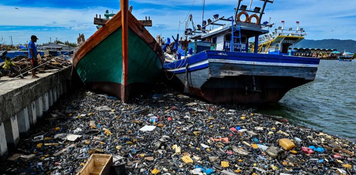 Un hombre observa basura y residuos plásticos flotando junto a barcos pesqueros en un puerto de Banda Aceh en Indonesia.