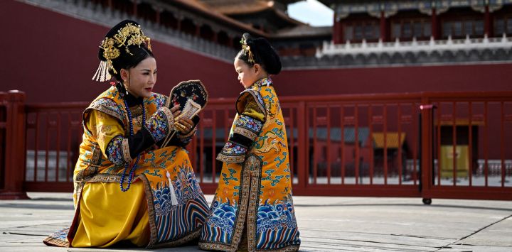 Una mujer y una niña vestidas con un traje tradicional chino charlan junto a la Ciudad Prohibida durante una sesión de fotos con un fotógrafo local en Pekín.