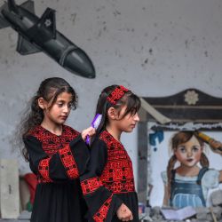 Una niña palestina peina el cabello de otra mientras posan ante un mural durante una exposición de arte mixto titulada "la ocupación mata a la infancia" que tiene lugar entre los escombros de las casas destruidas por los ataques aéreos israelíes durante el conflicto de mayo de 2023 en Deir al-Balah, en el centro de la Franja de Gaza. | Foto:MOHAMMED ABED / AFP