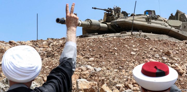 Clérigos musulmanes libaneses suníes y chiíes hacen gestos hacia un carro de combate israelí Merkava desplegado a través de la alambrada de espino que delimita la "línea azul" -trazada por las Naciones Unidas para marcar la retirada de Israel del sur del Líbano en 2000- en una posición a lo largo de la frontera cerca del pueblo de Kfar Shuba, en el sur del Líbano.