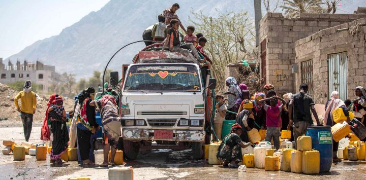 En esta imagen la gente se reúne con bidones para llenar agua de un camión cisterna en las afueras de la tercera ciudad de Yemen, Taez.