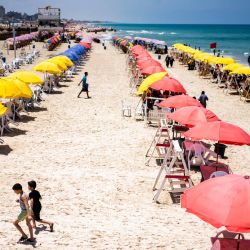 Palestinos caminan junto a las sombrillas que cubren la playa en la ciudad de Gaza. | Foto:Jewel Samad / AFP