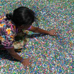 Un trabajador arregla chips de plástico procesados hechos de botellas de plástico recicladas en una instalación de reciclaje de plástico en Panagoda, Sri Lanka. | Foto:ISHARA S. KODIKARA / AFP