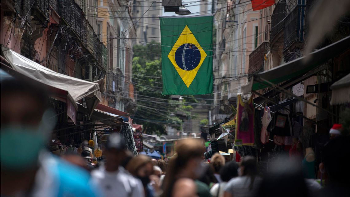 People walk at a market under a Brazilian flag in downtown Rio de Janeiro, Brazil, on December 8, 2020.