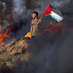Un joven palestino sostiene una bandera junto a neumáticos ardiendo durante una protesta junto a la valla fronteriza con Israel, al este de la ciudad de Gaza. Israel ha intensificado sus operaciones en el norte de Cisjordania, donde se encuentran la ciudad de Yenín y su campo de refugiados adyacente, bastión de grupos armados palestinos en el que se ha producido una oleada de ataques contra israelíes, así como ataques de colonos judíos contra comunidades palestinas. | Foto:MAHMUD HAMS / AFP