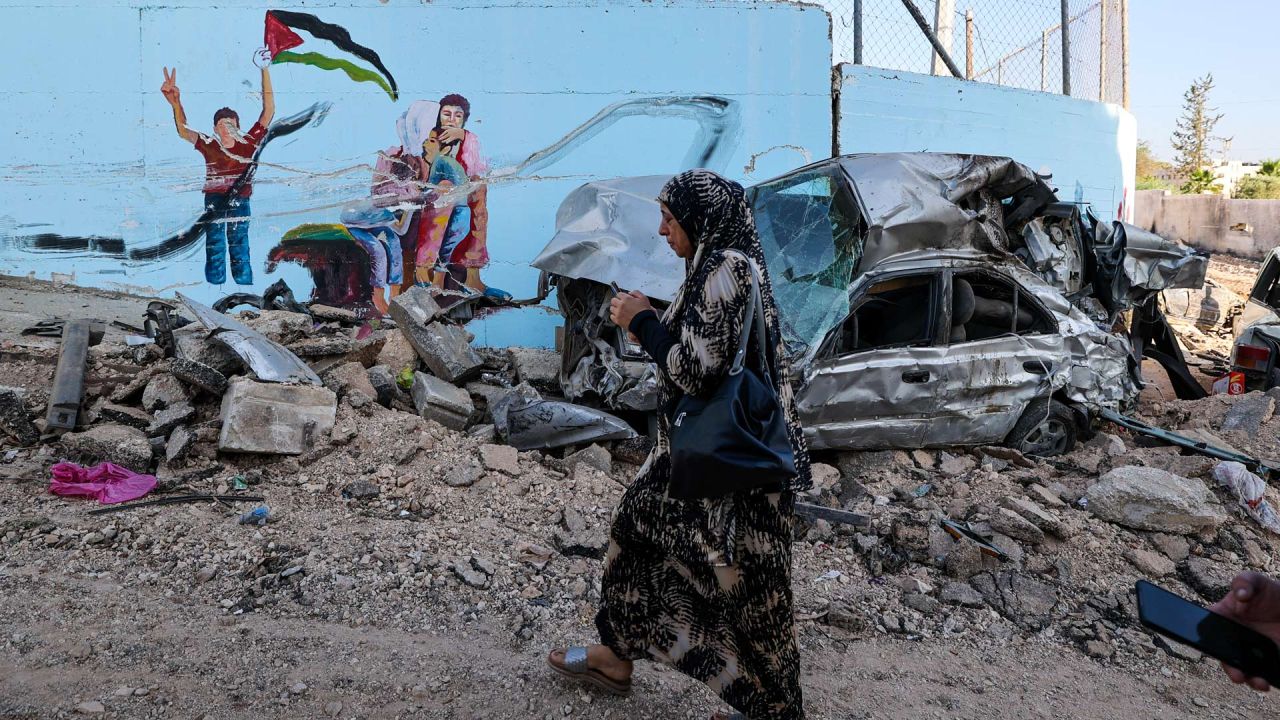 Una mujer pasa junto a los restos de un coche en una calle de la ciudad ocupada de Yenín, en Cisjordania, después de que el ejército israelí declarara el fin de una operación militar de dos días en la zona. El ejército israelí lanzó la incursión en el campo de refugiados de Yenín durante la cual murieron 12 palestinos y un soldado israelí. | Foto:JAAFAR ASHTIYEH / AFP