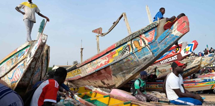 La gente se pone de pie y se sienta en piraguas estacionadas en la playa en un muelle de pesca, en Mbour. Foto SEYLLÚ / AFP