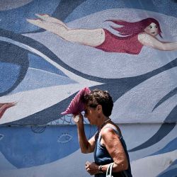 Una persona se protege del sol con un ventilador de mano mientras pasa junto a un mural de los artistas Maria Ginzburg y Gaetano Matrella, en el centro de Roma. Foto Tiziana FABI / AFP | Foto:AFP