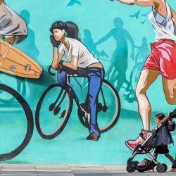 Una mujer empuja un cochecito infantil frente a un mural que representa atletas corriendo y montando en bicicleta cerca de la playa de Jumeirah en Dubái. | Foto:KARIM SAHIB / AFP