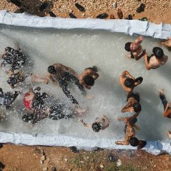 Esta imagen aérea muestra a personas nadando en una piscina improvisada en medio de altas temperaturas en un campamento para desplazados internos en Zaradna, en la provincia de Idlib, en el noroeste de Siria, controlada por los rebeldes. | Foto:AAREF WATAD / AFP