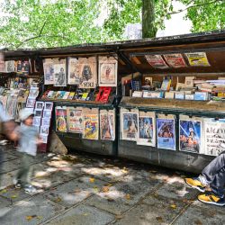 Un Bouquinistes de París se sienta en su puesto de venta de libros antiguos y carteles antiguos exhibidos a lo largo de las orillas del río Sena, en París. | Foto:MIGUEL MEDINA / AFP