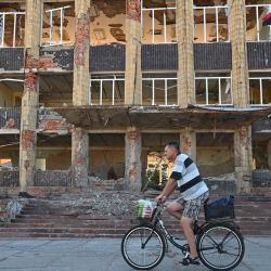 Un residente local circula en bicicleta frente a un edificio destruido en la ciudad de Kupiansk, región de Kharkiv, en medio de la invasión rusa de Ucrania. | Foto:SERGEY BOBOK / AFP