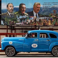Un viejo automóvil estadounidense pasa cerca de un cartel del difunto líder cubano Fidel Castro, el expresidente Raúl Castro y el actual presidente Miguel Díaz-Canel en La Habana. | Foto:YAMIL LAGE / AFP