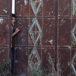 Un niño se asoma desde detrás de una puerta mientras un joven palestino enmascarado permanece de pie durante los enfrentamientos con las fuerzas israelíes mientras los soldados realizan una operación de búsqueda en la aldea de Baita, en la Cisjordania ocupada. | Foto:JAAFAR ASHTIYEH / AFP