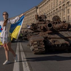 Una mujer posa para fotografías sosteniendo la bandera ucraniana junto a vehículos militares blindados rusos destruidos que se exhiben en la calle Khreshchatyk el Día de la Independencia de Ucrania en Kiev, en medio de la invasión rusa de Ucrania. | Foto:Roman Pilipey / AFP