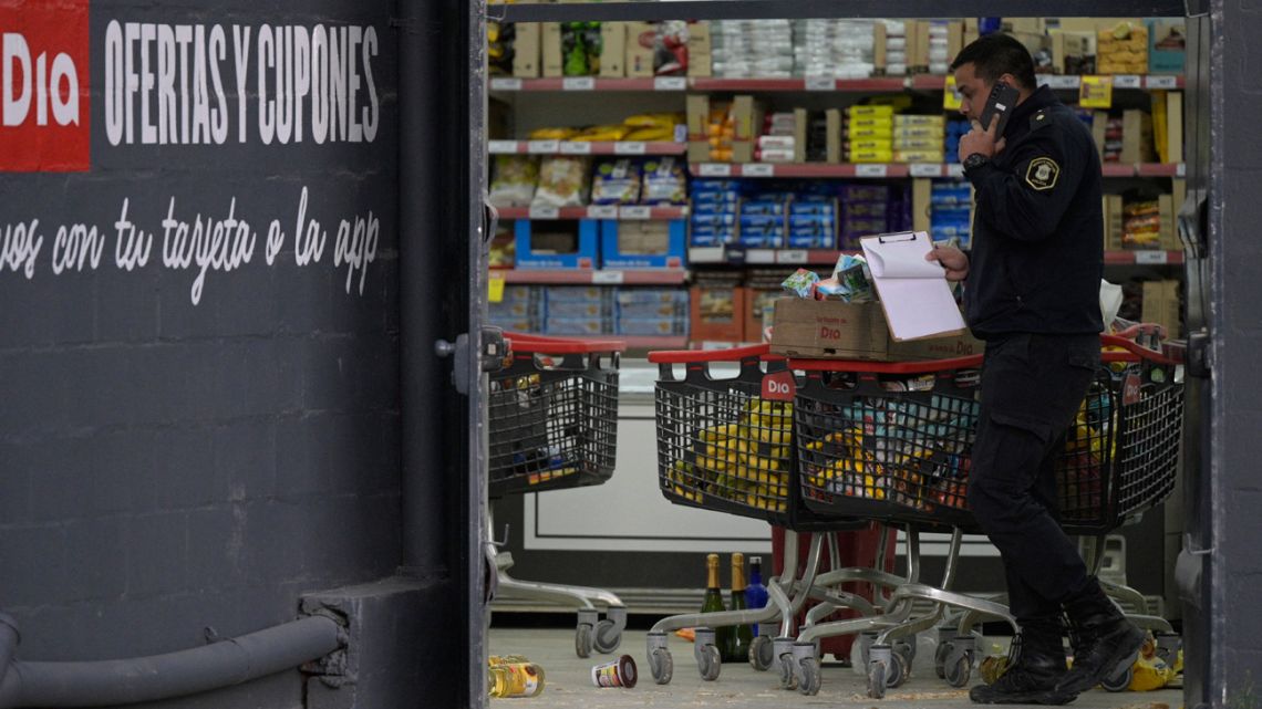 A Buenos Aires Province police officer speaks on a mobile phone next to a cart with merchandise at a Día supermarket after it was looted, in José C. Paz on the outskirts of Buenos Aires on August 22, 2023.  