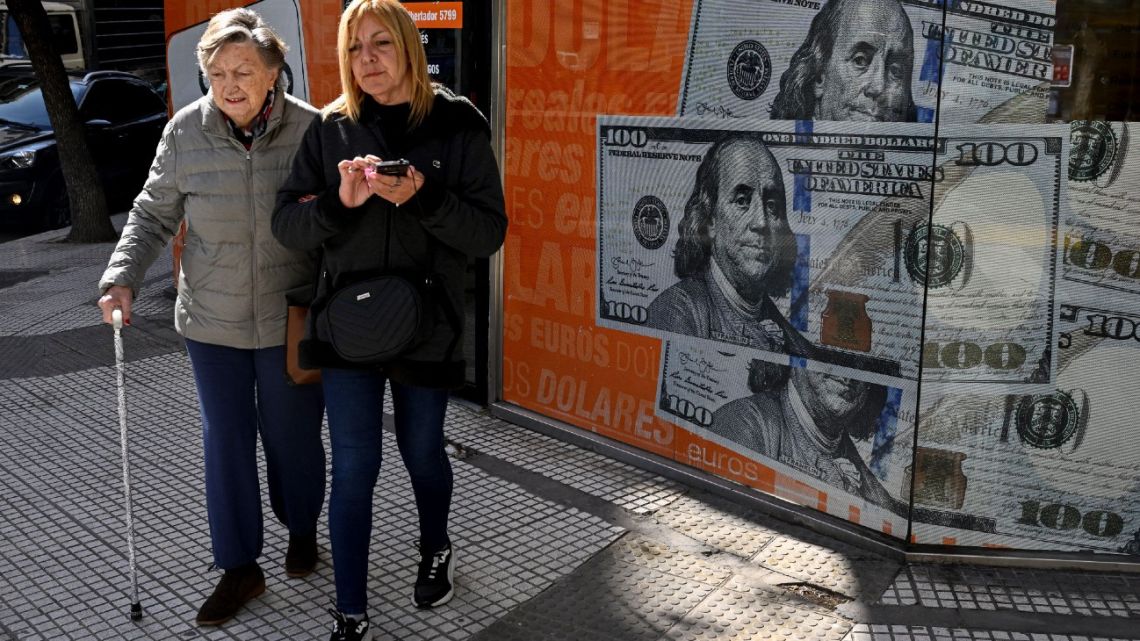 Women walk past an image of one hundred dollar notes in Buenos Aires on August 14, 2023, a day after primary elections in Argentina. 