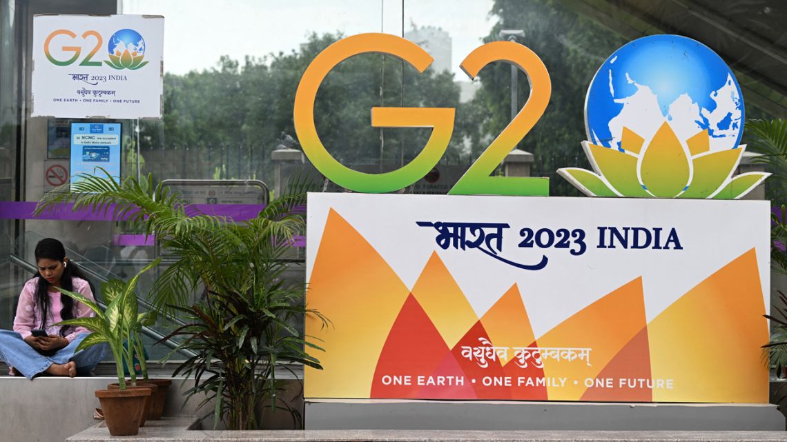 A woman sits near a G20 summit logo installed along a street in New Delhi on September 6, 2023. Special forces, bulletproof cars and men hired to chase away monkeys are among India's elaborate G20 preparations as Prime Minister Narendra Modi readies for a weekend in the global spotlight. 