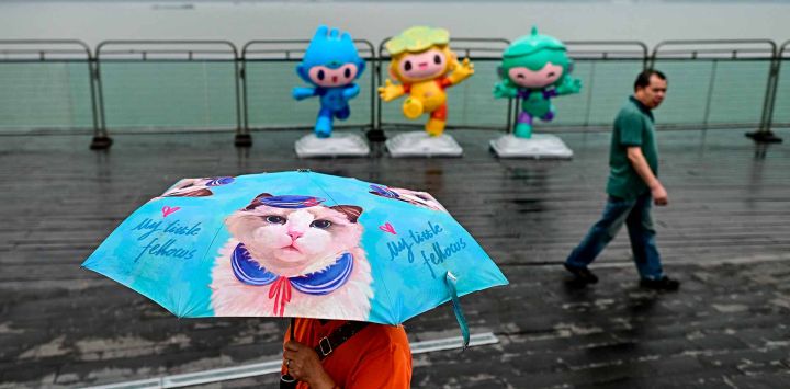 Una mujer que lleva un paraguas pasa junto a las mascotas de los Juegos Asiáticos, Chenchen. Foto de MANAN VATSYAYANA / AFP 