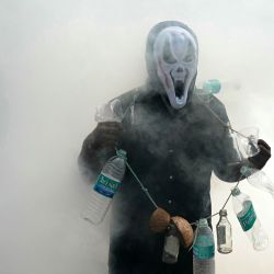 Un hombre usa botellas de plástico para crear conciencia sobre las enfermedades transmitidas por mosquitos mientras los trabajadores municipales fumigan una localidad en Chennai, India. | Foto:R. Satish Babu / AFP