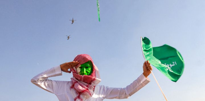 Un hombre que lleva una mascarilla pintada con los colores verde y blanco de Arabia Saudita saluda mientras asiste a un espectáculo aéreo que conmemora las celebraciones del 93º Día Nacional de Arabia Saudita en Riad.