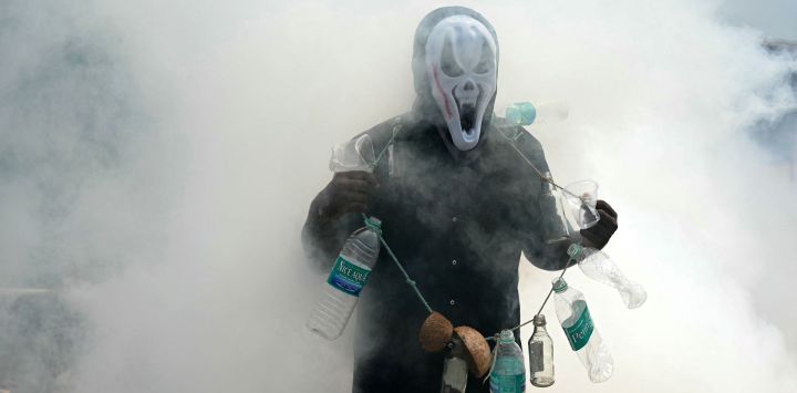 Un hombre usa botellas de plástico para crear conciencia sobre las enfermedades transmitidas por mosquitos mientras los trabajadores municipales fumigan una localidad en Chennai, India.