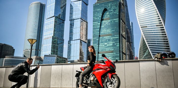 Un hombre toma una fotografía de una mujer posando en una motocicleta frente al Centro Internacional de Negocios de Moscú.
