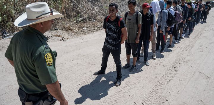 Migrantes de Venezuela hacen fila frente a un agente de la Patrulla Fronteriza de EE. UU. antes de caminar hacia un área de procesamiento después de cruzar el Río Grande en Eagle Pass, Texas.