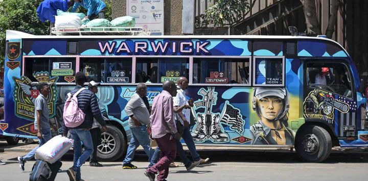 Los peatones caminan junto a un matatu, autobuses de propiedad privada utilizados como medio de transporte público. Nairobi. Foto de SIMON MAINA / AFP