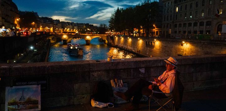 Un artista vende sus cuadros por la noche en el puente Petit Pont Petit Pont de París. Foto de Dimitar DILKOFF / AFP